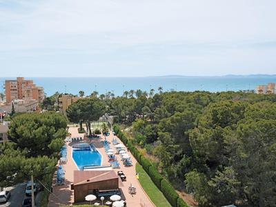 Helles Freibad mit blauer Wasserfläche, umgeben von grünen Bäumen und Gebäuden unter klarem Himmel.