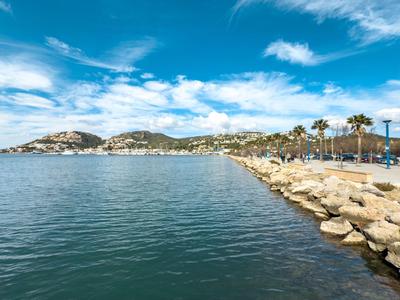 Klares Meer mit felsiger Küste, Palmen und Häusern unter blauem Himmel mit wenigen Wolken.