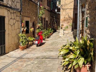 Enge gepflasterte Gasse mit Steinmauern, Pflanzen in Töpfen und rotem Motorroller.