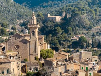 Blick auf ein Dorf mit einer Kirche und Häusern vor einem bewaldeten Hügel.