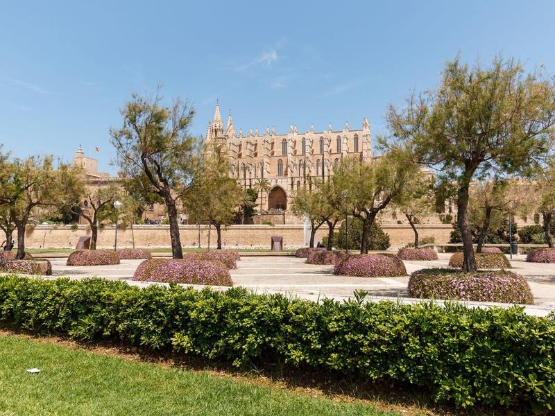 Großes historisches Gebäude mit Bogenfenstern, umgeben von Olivenbäumen und gepflegtem Grün.