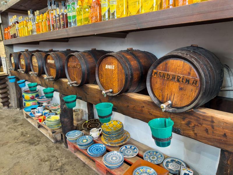 Reihe von kleinen Holzfässern auf einem Regal mit bunten Tassen und Tellern darunter.