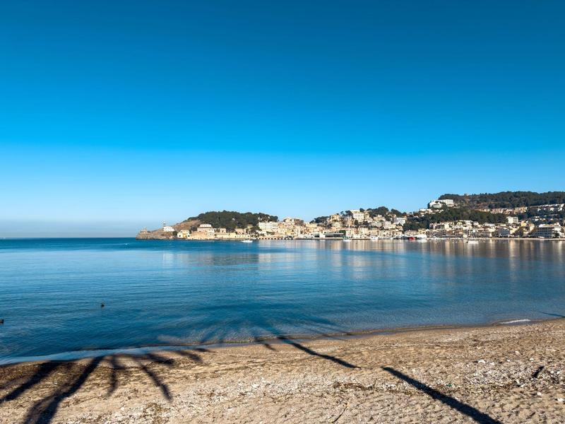 Strand mit Sand und Kies, ruhiges blaues Meer und Küstenstadt unter klarem Himmel.