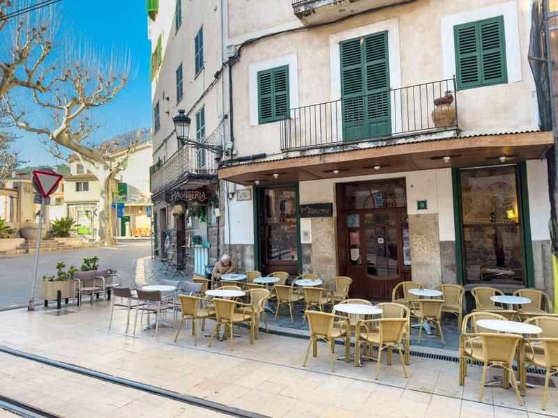 Leerer Außenbereich eines Cafés mit mehreren Tischen und Stühlen an einer hellen Gebäudefassade.