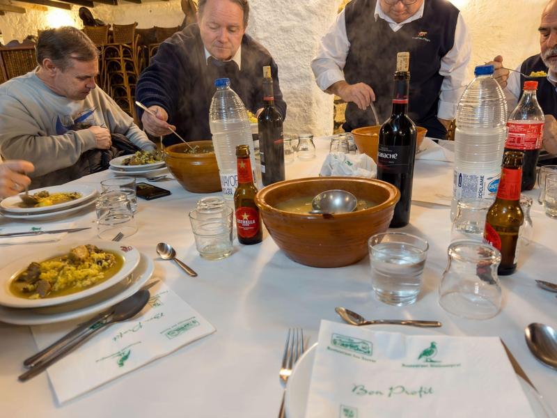 Mehrere Menschen sitzen an einem Tisch mit weißem Tischtuch, Tellern mit Essen, Getränken und Besteck.