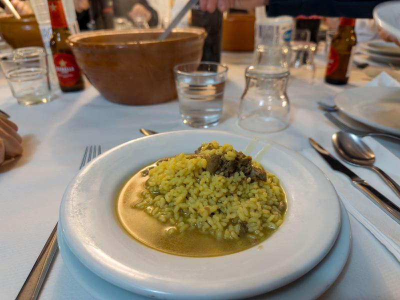 Ein Teller mit gelbem Reis und Fleisch auf einem gedeckten Tisch mit Gläsern und Besteck.