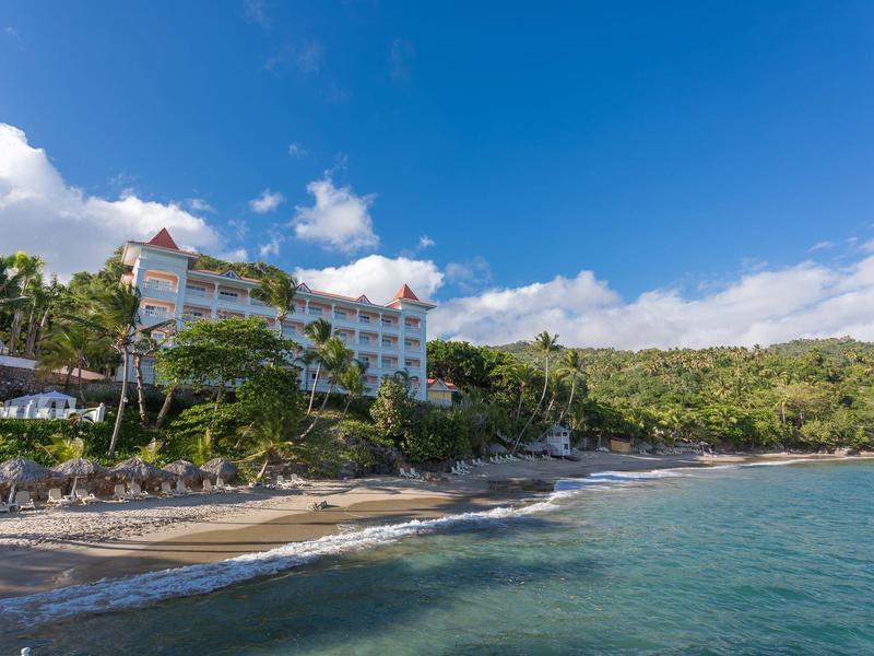Strand mit Baumgruppen, Wellen und mehrstöckigem Hotel unter blauem Himmel am Hang.