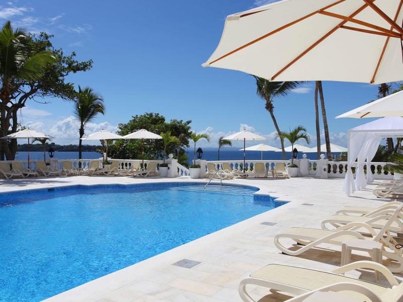Schwimmbad mit blauen Wasser, weißen Liegestühlen und Sonnenschirmen bei klarem Himmel am Meer.