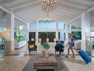 Helles Hotelfoyer mit hohen Decken, modernen Möbeln und zwei Personen, eine mit Koffer.
