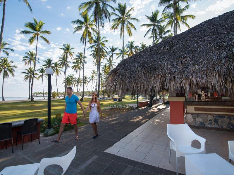 Ein Mann und ein Mädchen spielen Ball auf einer Terrasse neben einer Bar mit Palmen am Strand.
