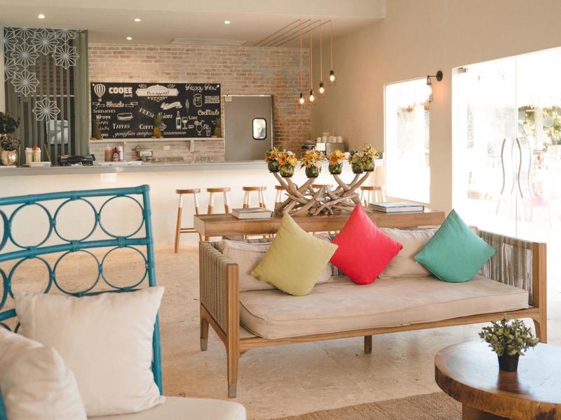 Helles, modernes Wohnzimmer mit hellen Holzmöbeln, bunten Kissen und großen Fenstern.