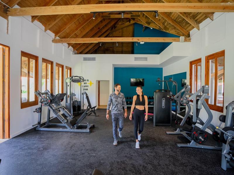 Fitnessraum mit Holzbalkendecke, großen Fenstern und zwei Frauen auf schwarzem Boden.