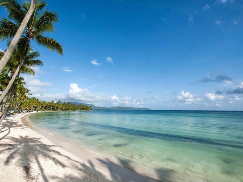 Strand mit weißem Sand, Palmen und klarem blauem Wasser unter blauem Himmel mit Wolken.