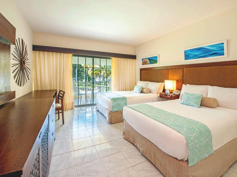 Hell eingerichtetes Hotelzimmer mit zwei Betten, großem Fenster und modernem Holzmöbel.