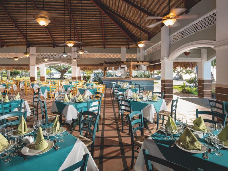 Weitläufiges Restaurant mit grün eingedeckten Tischen, Holzboden und offenem Dachstuhl aus Holz.