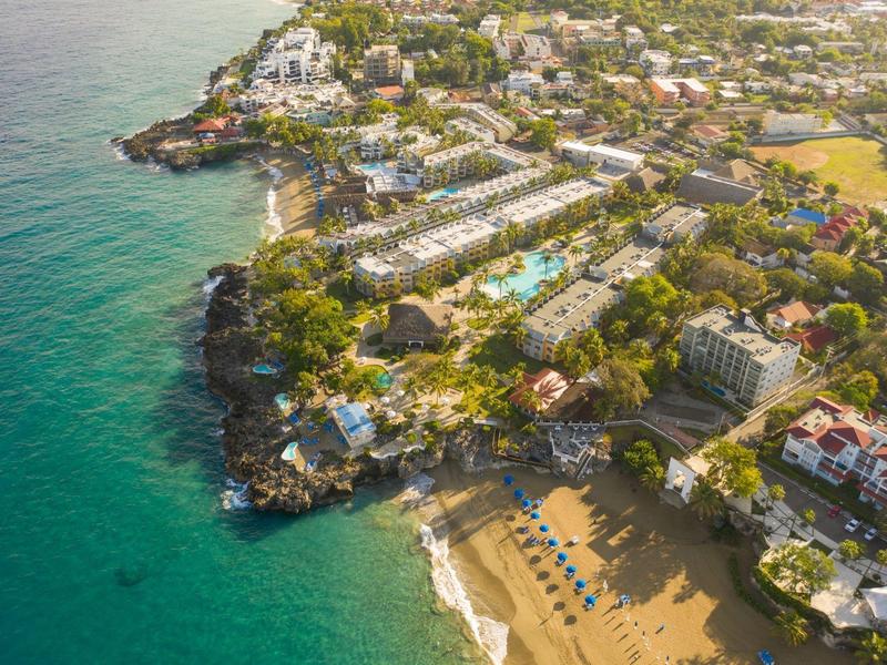 Küstengebiet mit türkisfarbenem Meer, Sandstrand, Sonnenschirmen und dicht bebautem Wohngebiet.