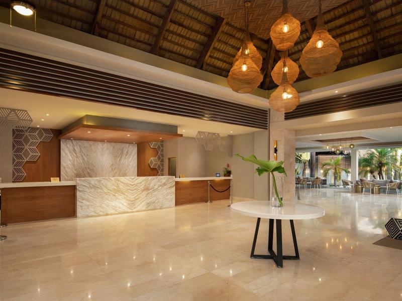 Große Hotelhalle mit Marmorboden, Rezeption aus Holz und Marmor, runden Lampen und Pflanze auf mittlerem Tisch.