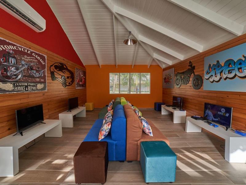 Innenraum eines bunten Spielzimmers mit Sitzbänken, Fernsehern und Fahrzeugmotiven an den Wänden.