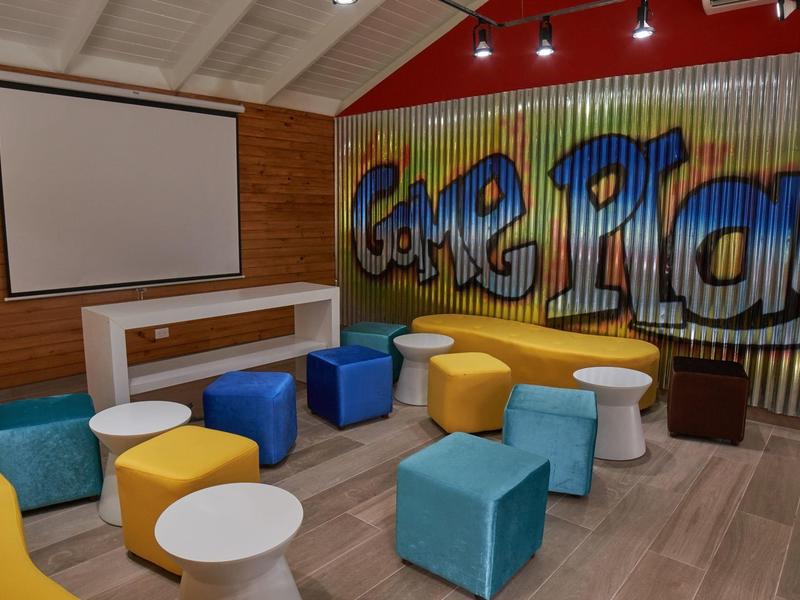 Buntes Gaming-Zimmer mit bequemen Sitzwürfeln, Graffiti-Wand und großer Leinwand in modernem Stil.