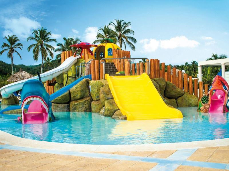 Bunter Wasserspielplatz mit Rutschen und Palmen in einem flachen Pool unter blauem Himmel.