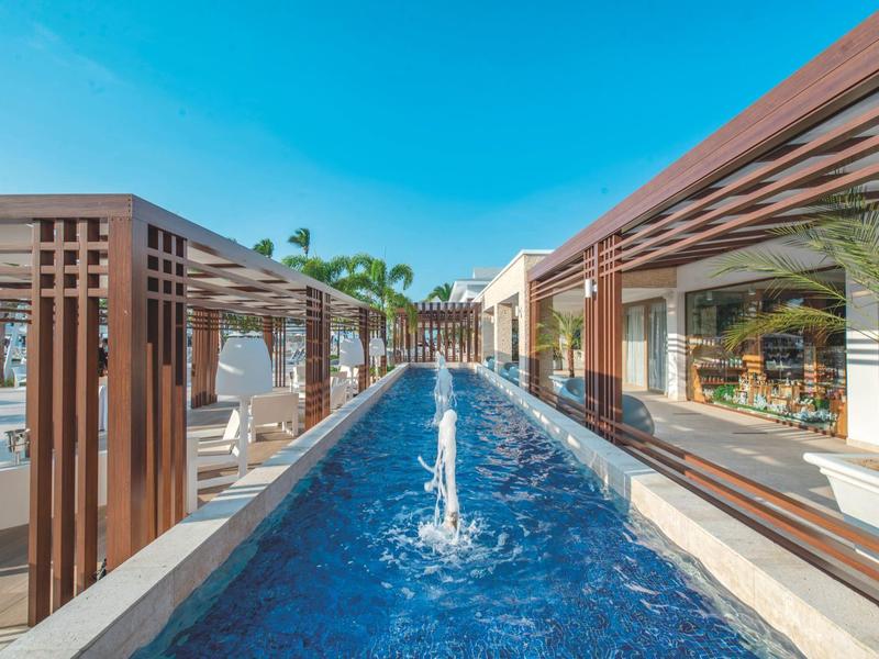 Moderner Außenbereich mit langem rechteckigem Wasserbecken, Holzpergolen und blauem Himmel.