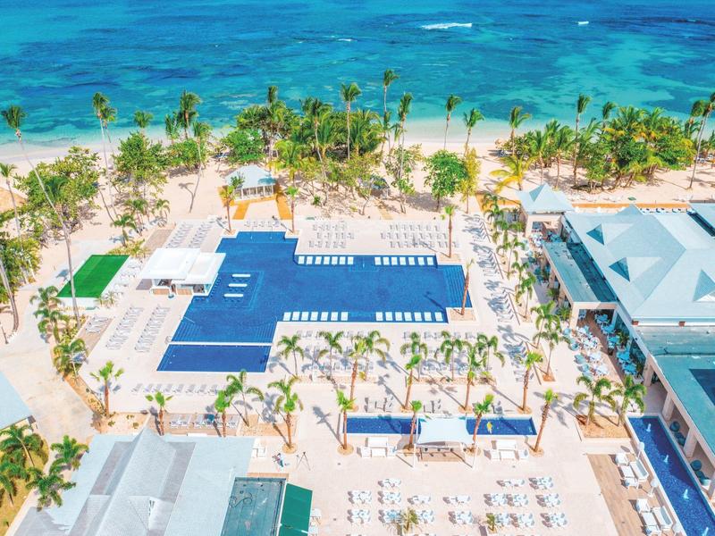 Strandresort mit blauem Pool, vielen Palmen und weißem Sand am türkisfarbenen Meer.