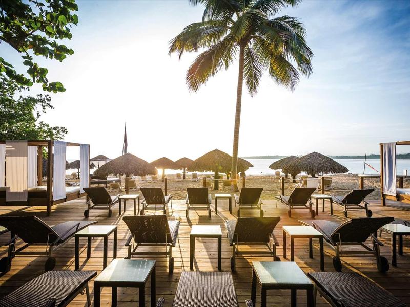 Strand mit Palmen, Sonnenliegen und Schirmen bei Sonnenuntergang am Meer.