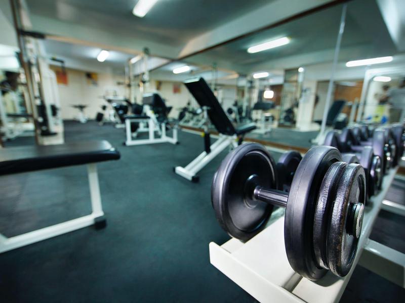 Helle Fitnessstudio mit Hanteln, Spiegeln, Bänken und verschiedenen Trainingsgeräten.