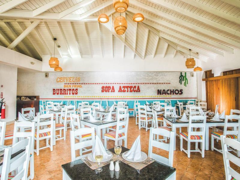 Hell beleuchteter Gastraum mit weißen Holzstühlen, Tischen und bunten Wandbeschriftungen.