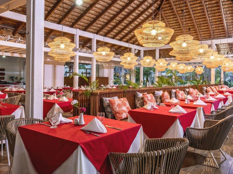 Restaurant mit roten Tischdecken, gefalteten Servietten, Holzstühlen und großen Lampen an Holzdach.