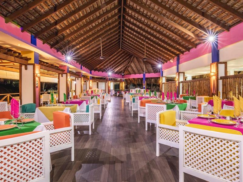 Großes, offenes Restaurant mit bunten Tischdecken und weißen Stühlen unter Holzdach.