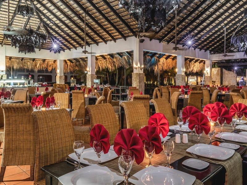 Großes, elegant dekoriertes Restaurant mit Rattanstühlen, weißen Tischtüchern und roter Blumendeko.