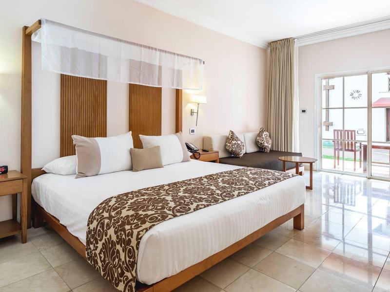 Helles Schlafzimmer mit großem Bett, Holzmöbeln, Marmorfliesen und Balkon mit Glas-Schiebetür.