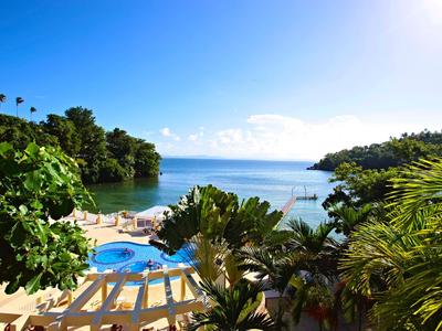 Blick auf eine tropische Hotelanlage mit Pool, Palmen und Meer unter klarem blauem Himmel.