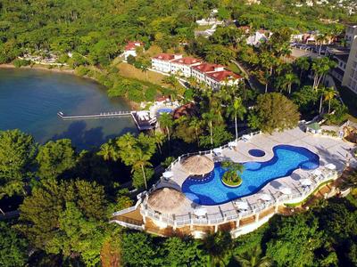 Aerial view of a hotel with pool in tropical surroundings next to a lake.