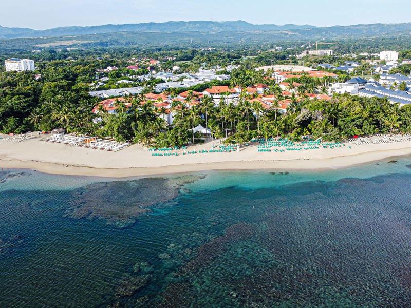 Luftaufnahme eines Resorts mit Sandstrand, grün bewaldetem Ufer und klarem blauem Meer.