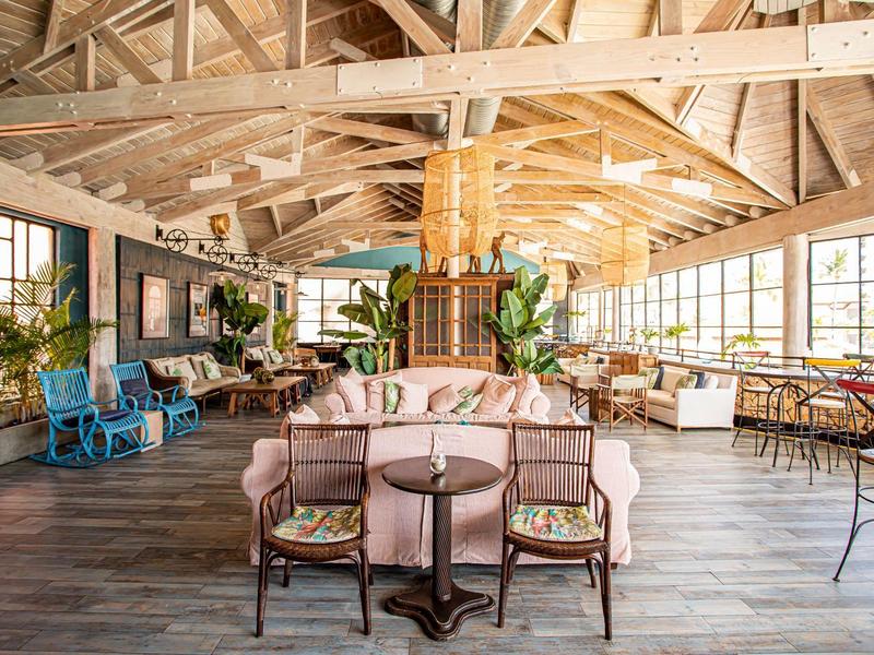 Großer, heller Raum mit Holzbalken, Pflanzen und gemütlichen Sitzgruppen aus Holz und Stoff.