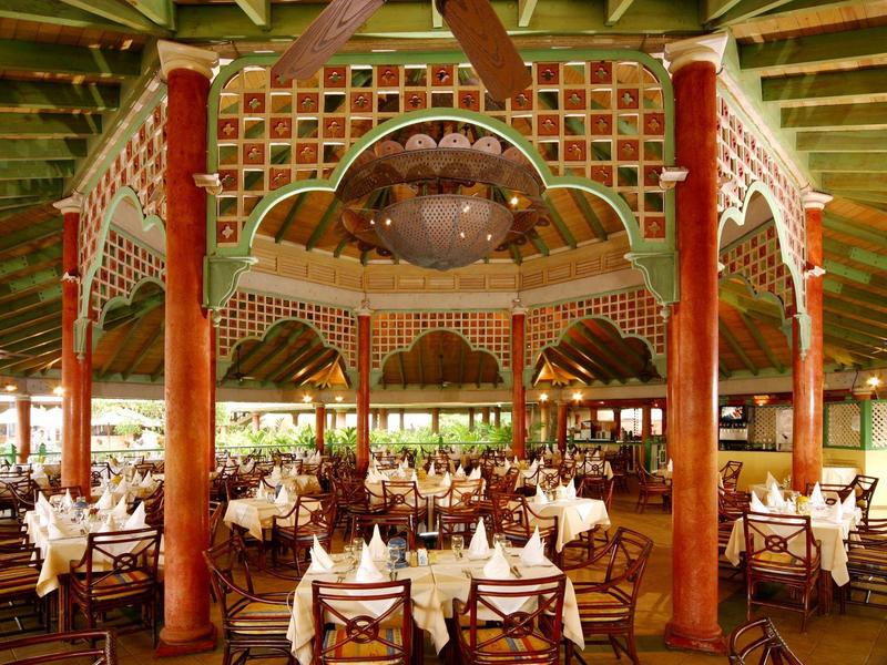 Großes, bunt dekoriertes Restaurant mit runden Tischen, weißen Tischdecken und Holzmöbeln.