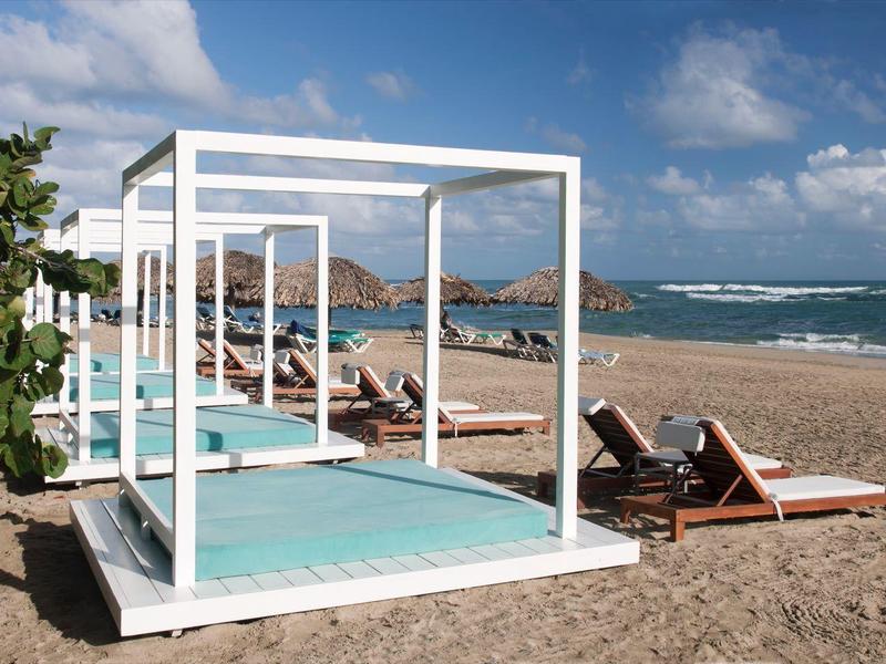 Strand mit weißem Pavillon, Sonnenliegen und Brise unter blauem Himmel mit Wolken.
