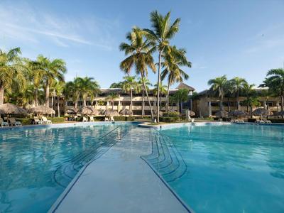 Großer Hotelpool mit Palmen umgeben und Liegestühlen bei klarem Himmel.