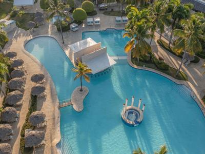 Großer Pool mit Insel und Liegebetten, umgeben von Palmen und Sonnenschirmen.