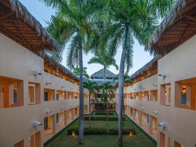 Hotel mit Innenhof, Palmengarten und zwei Stockwerken, beleuchtet bei Dämmerung.