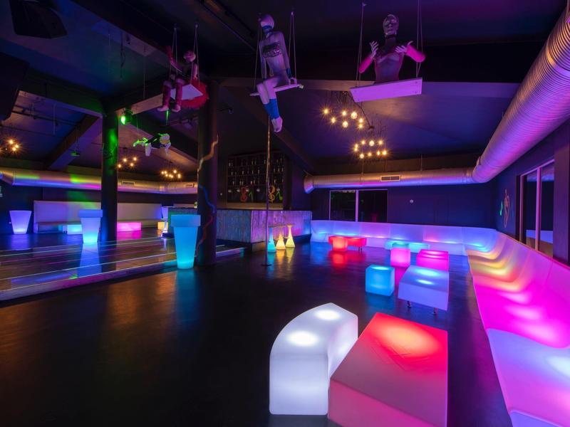 Moderner Club mit bunten LED-Bänken, Tanzfläche und Decken-Sitzen in dunklem Ambiente.