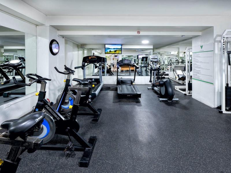 Fitnessraum mit stationären Fahrrädern, Laufbändern und Spiegelwänden in hellem, modernem Raum.