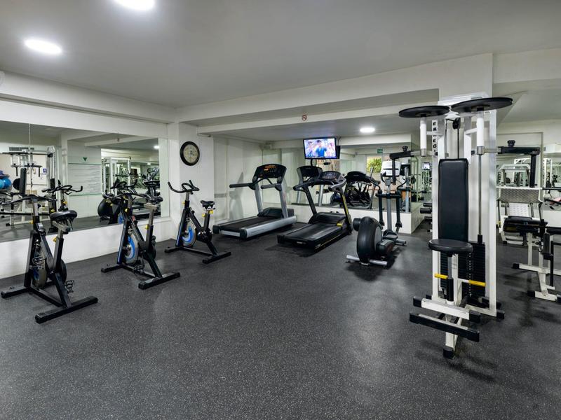 Großer, moderner Fitnessraum mit verschiedenen Trainingsgeräten und Spiegelwänden.