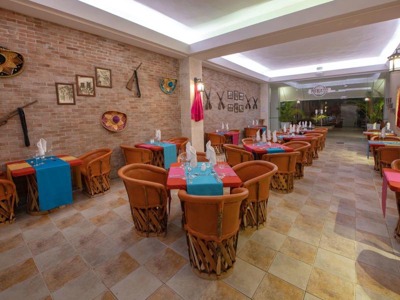 Hell eingerichteter Gastraum mit runden Holztischen, bunten Tischdecken und Stühlen aus Korbgeflecht.