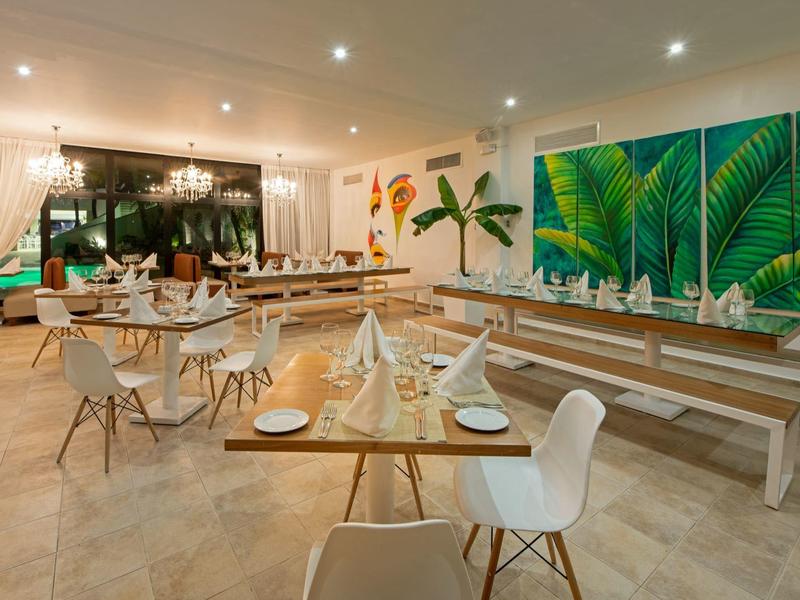 Modernes, helles Restaurant mit Holzstühlen, langen Bänken und großen Blätterbildern an der Wand.