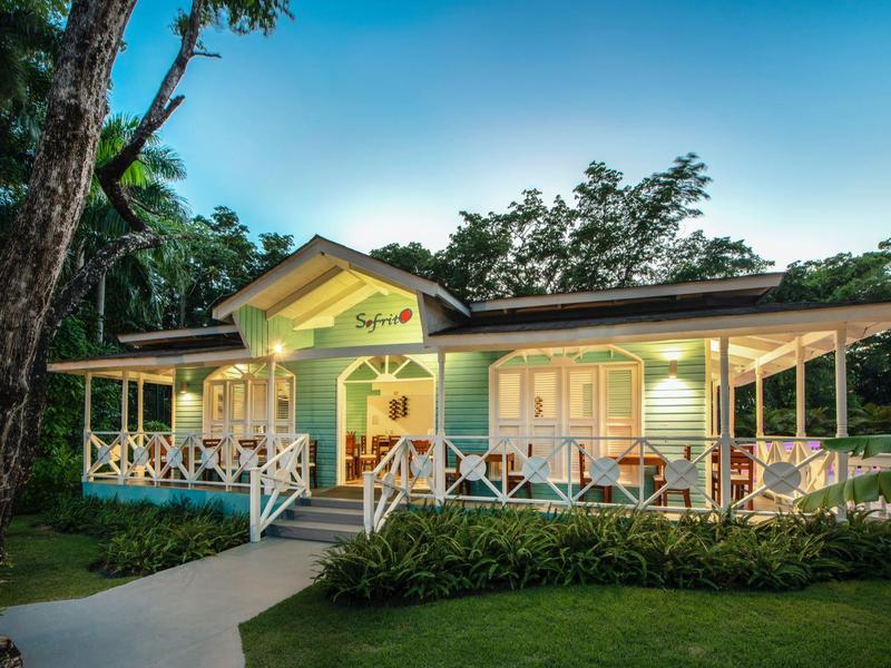 Einfamilienhaus mit breiter Veranda, grüner Fassade, weißen Holzgeländern und Beleuchtung bei Abenddämmerung.