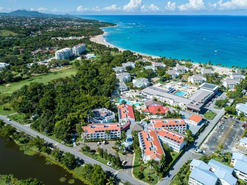 Luftaufnahme einer Küstenstadt mit blauen Meer, grünen Bäumen und weißen Gebäuden mit roten Dächern.