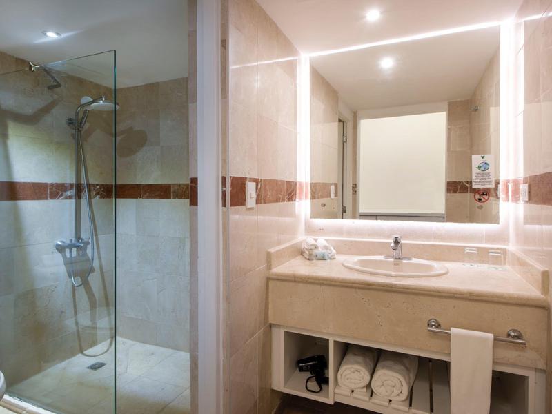 Moderner Badezimmerspiegel mit beleuchtetem Spiegel und Waschbecken neben einer gläsernen Duschtür.